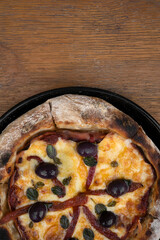 Pizza. Top view of a pizza with mozzarella cheese, grilled red bell peppers, ham, black olives and fresh oregano leaves, on the wooden table.