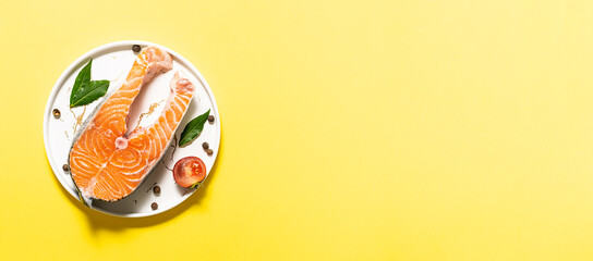 Fresh raw salmon steak with spices and herbs on bright yellow background long banner format. Copy space for your design. Food blog or cooking book cover template.
