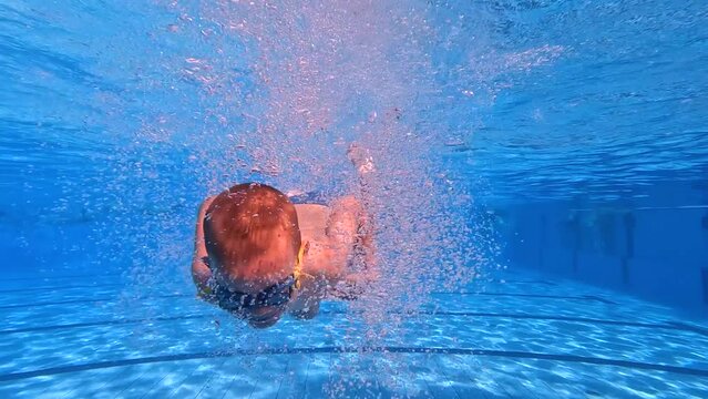 Underwater view of young boy with swimming goggles jumping and diving in the swimming pool. Slow motion 4k.