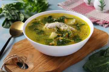 Soup with chicken, spinach and egg in a white bowl on a wooden board close-up