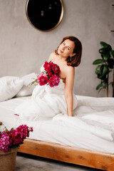 attractive topless woman with a bouquet of peonies in a blanket on the bed.