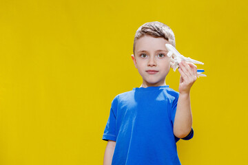 Little boy in a blue T-shirt holds a toy white plane and plays on a yellow background. Copy space. Travel concept