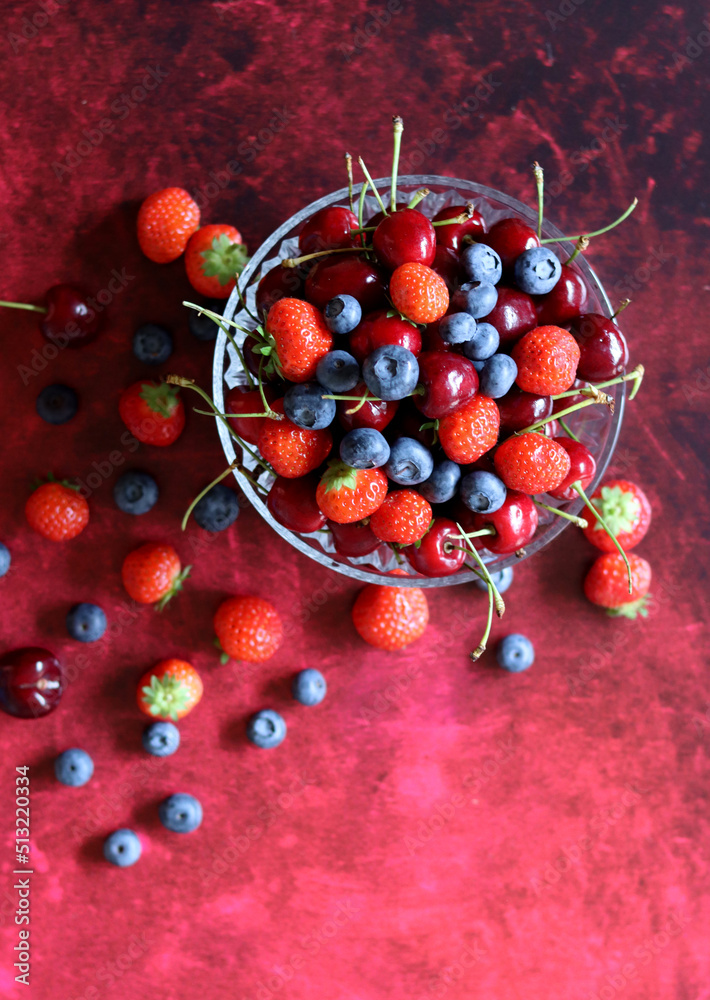 Poster Top view photo of berries in a glass bowl. Vibrant colors of Summer. Red background with copy space. Natural antioxidants concept. 