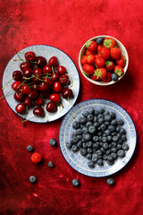Summer still life with fresh berries on ceramic plates. Top view photo of organic cherry, blueberry and strawberry. Healthy eating concept. 