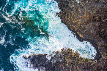 aerial view top down of ocean waves breaking on rocky coast 