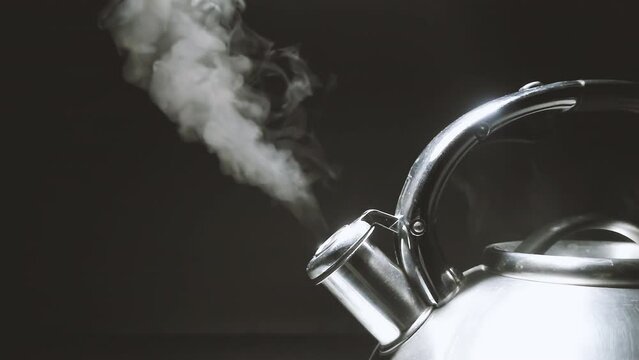 Boiling steel silver kettle with a whistle with steam close-up on a black background. 4k raw slow motion video 60 fps.