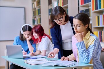 Group of teenage students and teacher study at desk in library