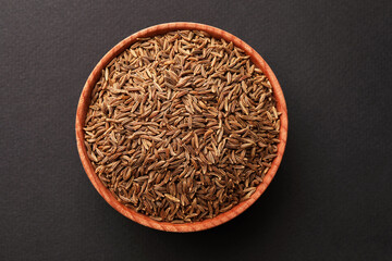 Fototapeta na wymiar Wooden bowl with cumin seeds on dark background, top view
