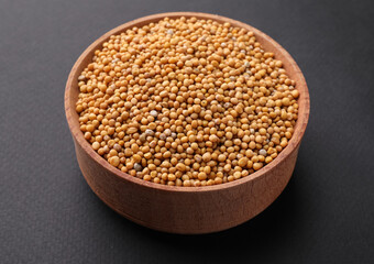 Wooden bowl with mustard seeds on grey background