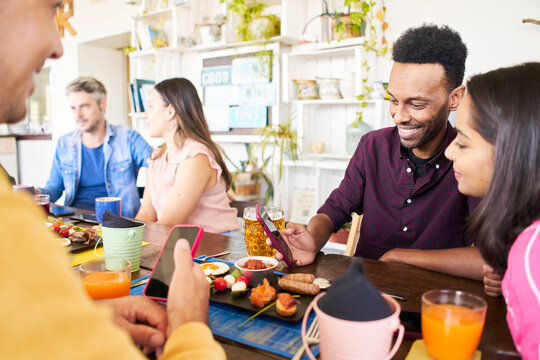 Man and woman watching something in a cell phone. Group of people using phone smiling in a cafe bar. Friends having breakfast and community concept