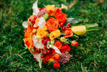 Stylish autumn wedding bouquet in very bright colors lies on the lush green grass. Wedding floristry idea.