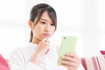 部屋でスマホを見る女性　考える