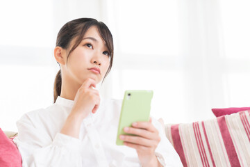 部屋でスマホを見る女性　考える