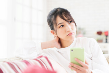 部屋でスマホを見る女性　考える