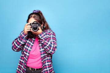Young curvy latina woman holding reflex camera and taking a photo. Indoor studio shot isolated on...