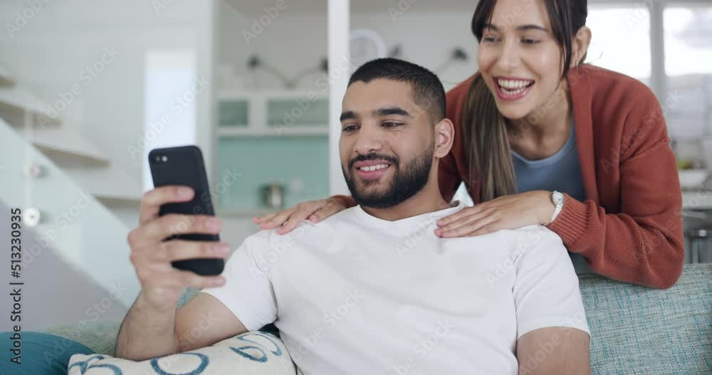 Sticker A young couple using a phone browsing online while kissing on the couch at home. Cheerful girlfriend giving her boyfriend a kiss while using social media together at home. Husband and wife bonding