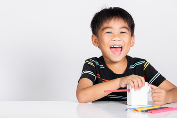 Fototapeta premium Little cute kid boy 5-6 years old smile using pencil sharpener while doing homework in studio shot isolated on white background, Asian children preschool sharpening color pencils, education concept