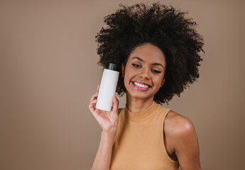 Beauty Latin woman with afro hairstyle. Brazilian woman. Holding blank shampoo packaging. Curly...