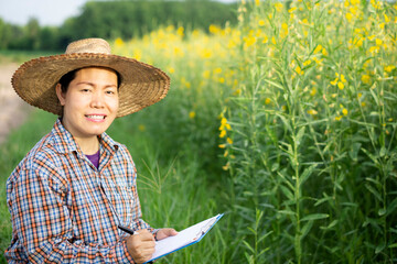 Portrait of Asian middle-aged woman gardener is at flower garden, surveying or checking diseases and growth of plants. Concept : research for develop and solve Agriculture problems. Field researcher. 