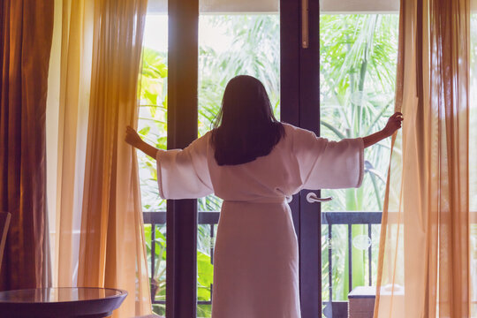 Asian women are staying in a hotel room after wake up on morning. Open the curtain in the room looking to outside view.Concept of traveling and resting happy in good hotel.