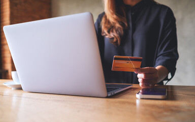 Closeup image of a woman holding credit card while using laptop and smart phone for online payment