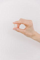 A single white pill being held by a women on a white backdrop.
