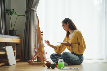 Young female painting on canvas in living room at home. Hobby and leisure concept.