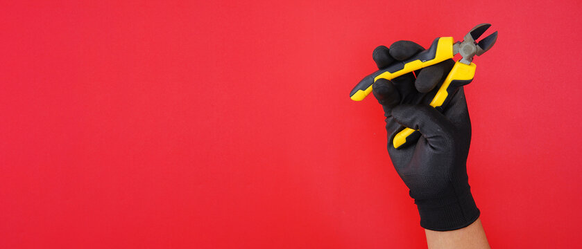 hand wearing blacke gloves holding diagonal pliers cutter isolated on a red background