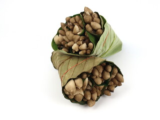 Ready-to-cook termite mushrooms wrapped in leaves isolated on white background.