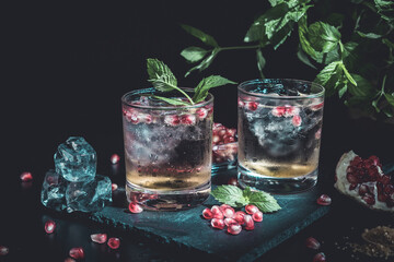 two colorful summer cocktails with pomegranate and mint on a black table