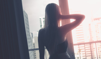 Fototapeta na wymiar Asian woman with seductive clothing is looking out o Bangkok City from apartment balcony. silhouette sunlight,