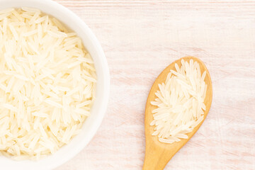 Long Basmati rice in ceramic bowl and spoon on brown wooden background. Macro. Flat lay. Diet food concept