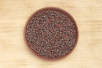 Spice Mustard seeds (Brassica juncea) in brown clay plate on wooden background. Close up. Vegetarian food concept
