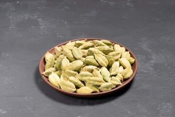 Spice green cardamom (Elettaria cardamomum) in clay plate on black concrete background. Macro. Healthy eating concept