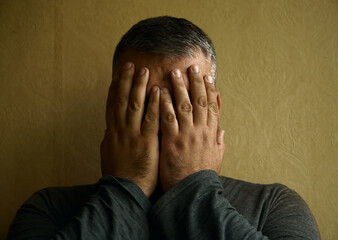 Man peers through his fingers. male  against  wall covering face with hands and peering out. Scared...