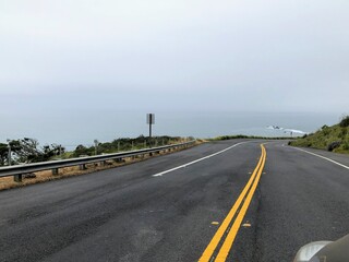 A closeup view of the highway 1 road along the rugged shoreline of the northern california  with rugged endless views of the ocean, cypress trees, and rocky cliffs