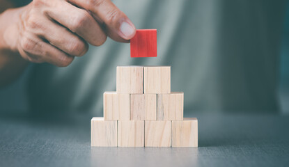 The young man was putting the red wooden blocks on top of the other wooden blocks.