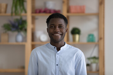 Obraz premium Head shot portrait successful young African businessman wear casual blue shirt smile looks at camera pose at workplace in cozy office. Professional occupation person, teacher profile picture concept