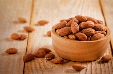 Almond kernels in wooden bowl on rustic dark wooden table.
