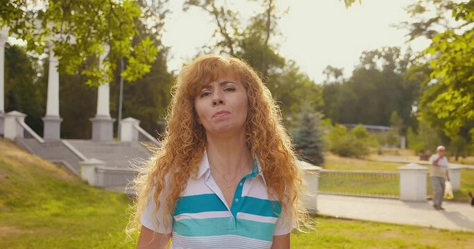 A happy blonde woman dances and sings in the park at sunset. A smiling woman sings standing outside feeling free and happy.