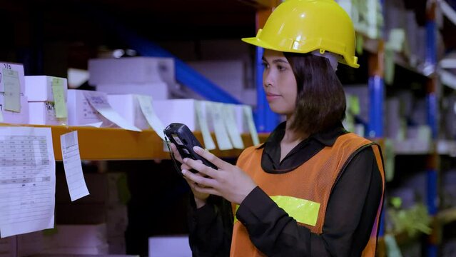 A beautiful female worker in uniform with her safety helmet on is holding scanner scanning parcel barcode in the warehouse store background. Inventory digitalization with barcode scanner concept.