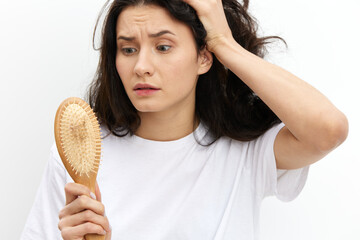 a sad, upset woman stands holding her head in panic and looks at a wooden massage comb