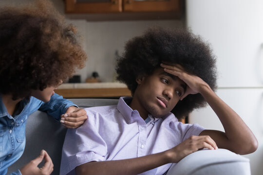 Teen African girl express her claim in aggressive manner to boyfriend sit nearby looks annoyed, ignoring girlfriend, feels disinterested to sort out their relationships. Bad relations, quarrel concept