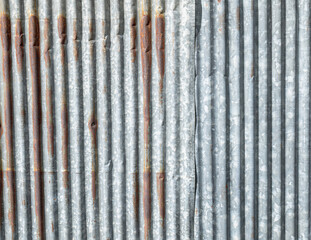 Old galvanized walls rusted and decayed due to sun exposure and rain, causing the surface to be rough and discolored.