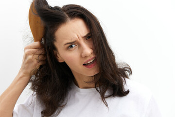 a sad, upset woman is trying to comb her long, dark, tangled hair with a wooden massage comb with a very sad, sad face