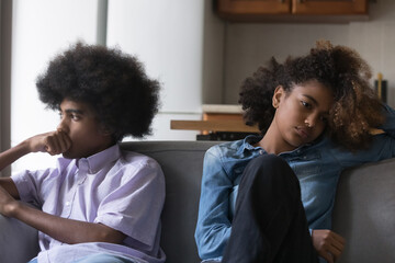 Sad silent African teenagers couple after fight sit apart on sofa, avoid talk, think about break...