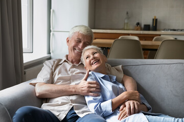 Joyful senior couple enjoy rest and conversation sit on cozy sofa, having warm harmonic relationship, happy marriage and endless love. Elderly homeowner family spend leisure at modern own home concept
