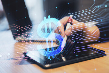 businessman hands using digital tablet on desktop with laptop and glowing dollar hologram on blurry background. E-commerce, online banking, cryptocurrency and finance concept. Double exposure.