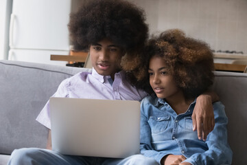 African girlfriend and boyfriend sit on sofa at home with laptop, discuss purchase, choose on-line movie on digital streaming TV services platform, young generation use modern tech, internet concept