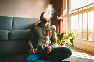 Man smoking bong and exhaling the smoke at home. Man smoking pot, medical marijuana or cannabis...